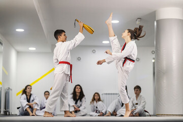 Taekwondo boy and girl are practicing kick on training and other teammates are watching them.