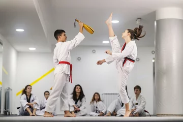 Deurstickers Taekwondo boy and girl are practicing kick on training and other teammates are watching them. © dusanpetkovic1