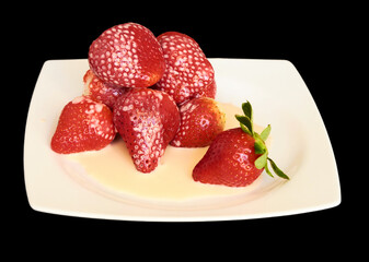 Ripe strawberries covered with yogurt on a square white plate on a black background