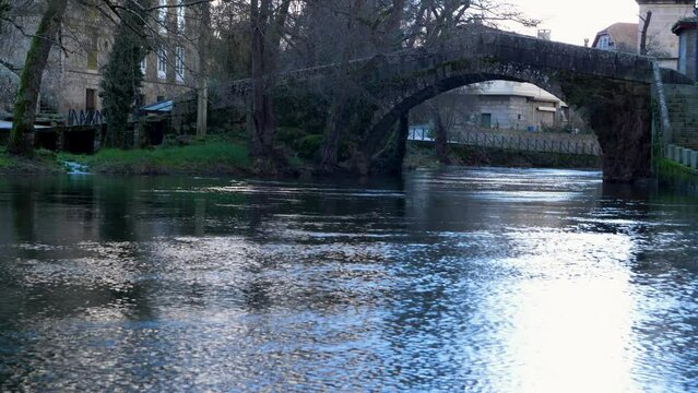 Water shimmers as it flows and light reflects bright off it fronting roman bridge