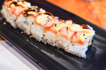 Sushi roll with salmon and drizzled sauce on a black plate.