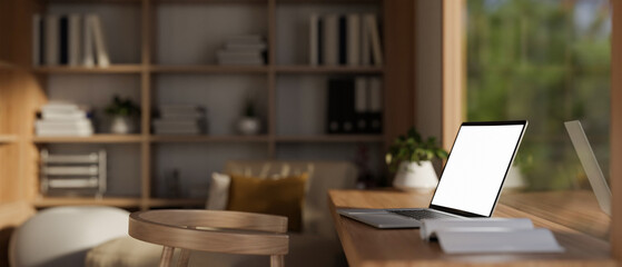 Side view image of a white-screen laptop computer on a wooden desk in a modern, Scandinavian room.