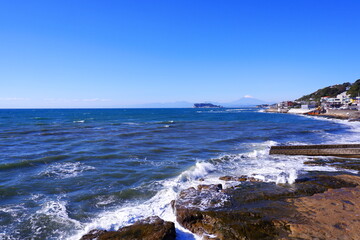 Fototapeta na wymiar 相模湾の荒波と江の島、冠雪した富士山の風景 