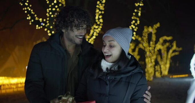 Young Indian man makes a gift to a woman on background of lights and garlands, New Year and Christmas concept