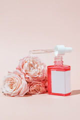 Beauty face oil in pink glass dropper bottle with flowers. Trendy shoot of cosmetics packaging. Essential oil with natural ingredients. Cruelty free cosmetics