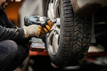An auto mechanic installing winter tires on car at vulcanizing workshop. - obrazy, fototapety, plakaty