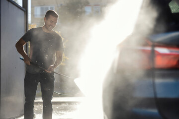 A happy man is washing his car at self-service car wash station.