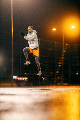 Fototapeta na wymiar An urban sportsman in shape is jumping high on snowy cold weather at night.