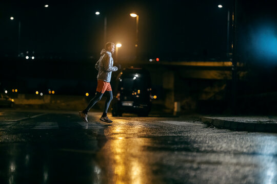 A night runner is running across the street at rainy weather.