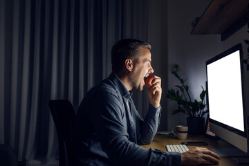 A healthy entrepreneur is eating apple while working at night at home office.