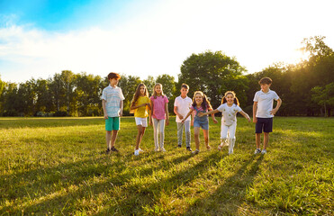 Group of a cute kids friends walking in the summer park. Happy girls and boys having fun and running outdoors. Smiling children in casual clothes spending time together on the lawn in nature.