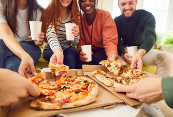 Happy smiling young people friends gathering in pizzeria or at home together eating tasty Italian food taking pizza slices from box enjoying party with cardboard cups in hands. Food delivery concept. - obrazy, fototapety, plakaty
