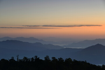 Colorful mountain range with tree line silhouette in foreground at sunset time