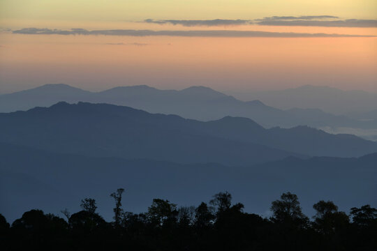 Colorful mountain range with tree line silhouette in foreground at sunset time