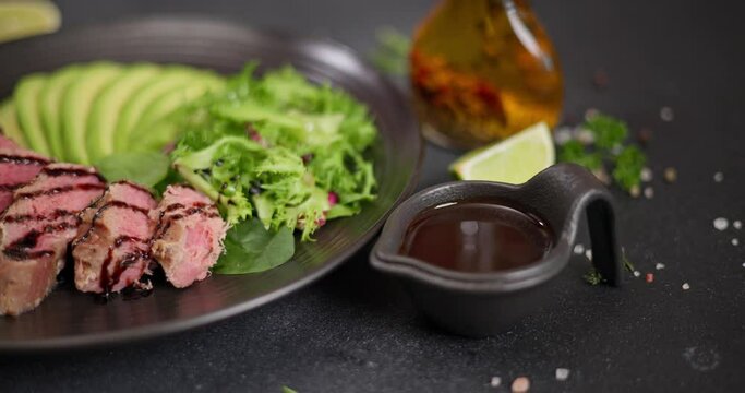 Sliced Grilled tuna steak with sliced avocado on a black stone serving board with teriyaki sauce