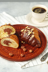 Chocolate croissant on clay plate with cup of coffee on table