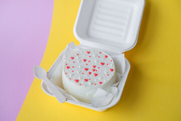 A box with a Valentine's Day bento cake with hearts stands on a pink and yellow background