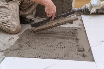 A construction worker applies cement for laying floor ceramic tiles with special spatula