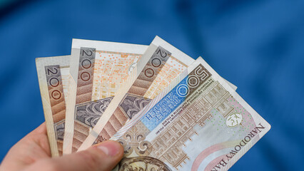 Polskie banknoty trzymane w dłoni, PLN na niebieskim tle © Paweł Kacperek