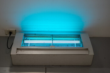 An insect or mosquito elimination device during turn-on the UV lighting which is installed on ceiling wall, the household electric equipment object. Close-up. © Nattawit