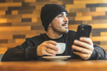 A man in a cafe drinks coffee and reads the news on the phone. Scrolling. Rest in a cafe. Leisure.