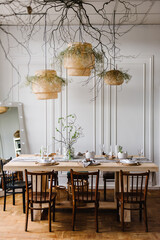 Happy easter dinner with decor at home. Minimalist composition in living room with copy space, hanging lamp, candle, easter eggs, vase with twig, branch, leaves. Interior design of easter dining room