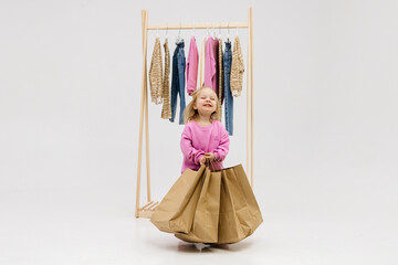 A child, a little girl, stands near the closet, chooses clothes against a light background. Dressing room with clothes on hangers. Wardrobe of children's and stylish clothes. Montessori wardrobe.