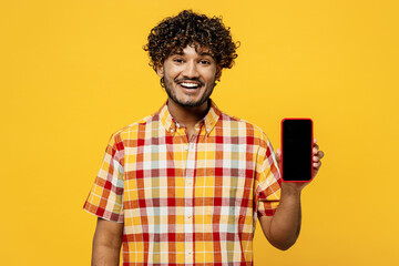 Young happy Indian man he wears shirt casual clothes hold in hand use mobile cell phone with blank...