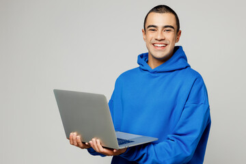 Side view young happy middle eastern IT man wear blue hoody casual clothes hold use work on laptop...