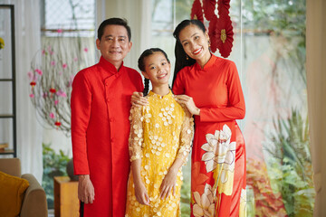 Fototapeta na wymiar Smiling parents and their teenage daughter wearing traditional costumes when celebrating Tet at home