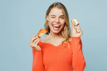 Deurstickers Close up young happy woman wear orange casual clothes look camera hold eat raw fresh sushi roll Japanese food with chopsticks wink isolated on plain blue background studio portrait. Lifestyle concept © ViDi Studio