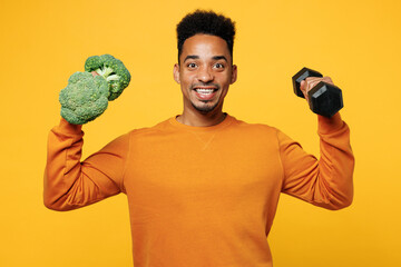Young excited man wear orange sweatshirt casual clothes hold in hand broccoli dumbbell isolated on...