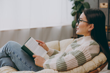 Side profile view young smart woman she wear casual clothes glasses sits on armchair read book...