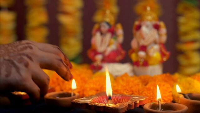 Indian woman hand placing diya in front of Hindu Gods - Diwali  idol worship  festival of lights  religious ritual. Family preparing for Deepawali puja - colorful flowers  Lord Ganesh  Devi Laxmi  ...