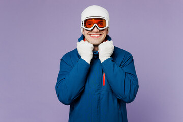 Smiling cool happy skier man he wear ski goggles mask hat touch warm blue windbreaker jacket collar looking camera spend extreme weekend winter season in mountains isolated on plain purple background.