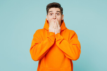 Young shocked surprised happy man he wears orange hoody casual clothes cover mouth with hand look...