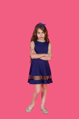 Full length of pensive little girl in blue dress arms crossed at pink isolated, thought looking at camera. Lovely emotional kid lady 9 year old, studio shot. Child emotion concept. Copy ad text space