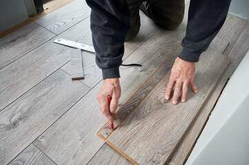 Close up of man construction worker with pencil in hand drawing line on laminate timber board. Male...