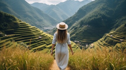 Rear view of a Vietnamese girl wearing a traditional white dress and hat walking on the mountain and golden rice terraces. Farming, farming, village life concepts.