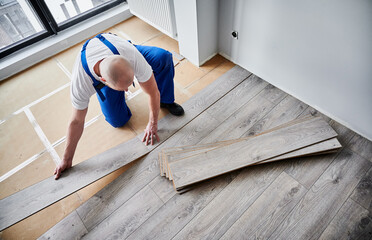 Top view of male construction worker laying laminate wooden planks on floor underlayment. Man in...