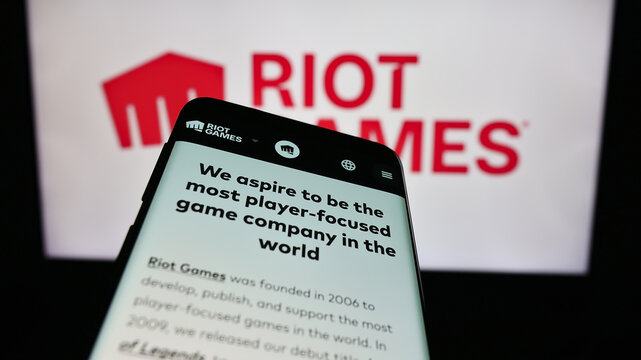 Stuttgart, Germany - 12-27-2023: Mobile phone with website of US video game development company Riot Games Inc. in front of business logo. Focus on top-left of phone display.