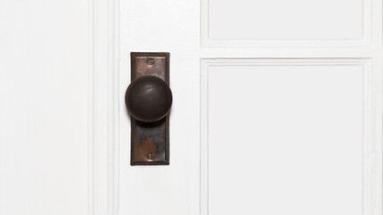 Close-up side view photo of an antique tarnished metal door handle on a white paneled wooden door with copy space.