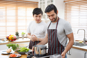 Fototapeta na wymiar LGBTQ+ gay bisexual cooking their meal together in the kitchen, LGBTQ gay couple making a spaghetti. A different ethnicity handsome gay couple enjoy cooking a spaghetti together in kitchen.