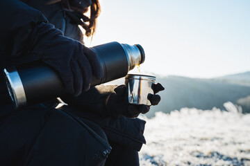 Concept of hot drinks, pouring brewed coffee into a mug, drinking hot tea outdoors in winter, hiking in the mountains, camping in the forest. - obrazy, fototapety, plakaty