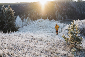 Winter adventure, guy walking along a trail in the mountains against the background of the glare of the morning sun, hiking in the forest, sunrise in the mountains.
