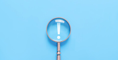 magnifying glass shows an icon exclamation mark on a blue background. points attention. concept of...
