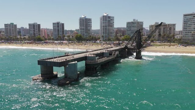 Aerial View Of Vergara Pier In Vina Del Mar With Hotel And Beach Coastline In Background. Pull Back Shot Over Turquoise Ocean Waters 