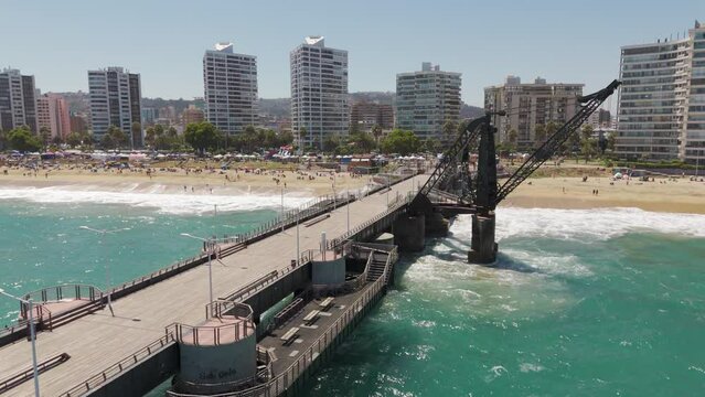 Aerial View Of Vergara Pier In Vina Del Mar. Push Forward Shot Past Crane With Hotel And Beach Coastline In Background 