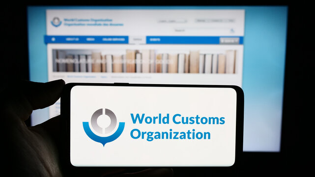 Stuttgart, Germany - 12-28-2023: Person holding cellphone with logo of World Customs Organization (WCO) in front of webpage. Focus on phone display.