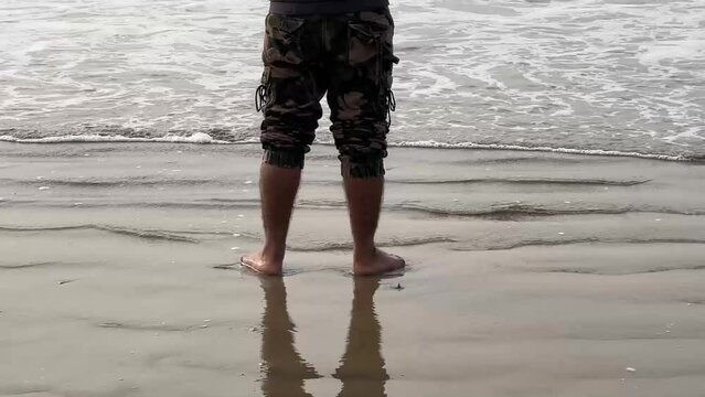 Close up shot of small waves touching persons feet in army half pant in a beach during daytime in  Bengal, India.